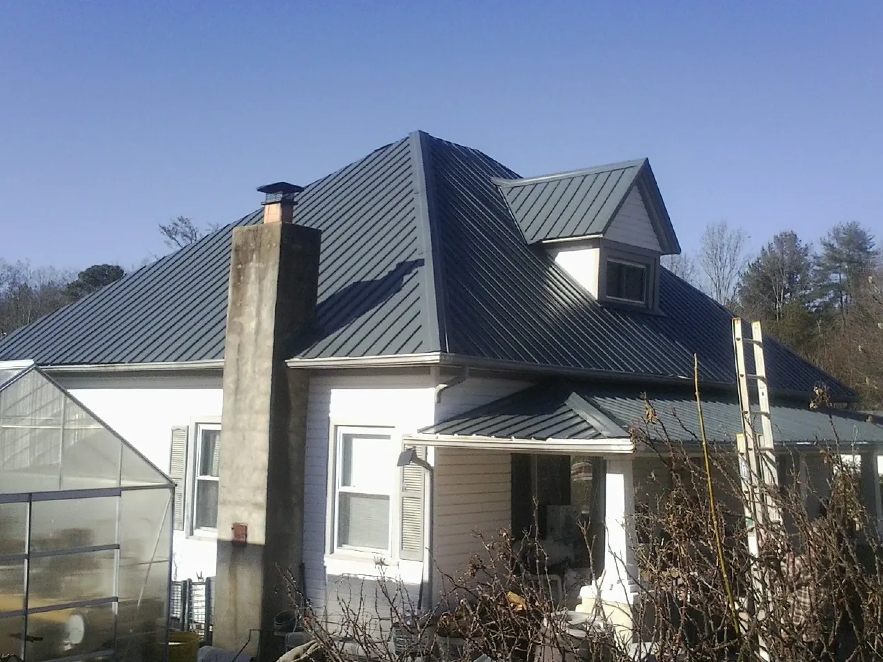 Dark blue standing seam metal roof on a white farmhouse with dormer — Slate & Tile Roof Repair by Roofing Brothers in Millen