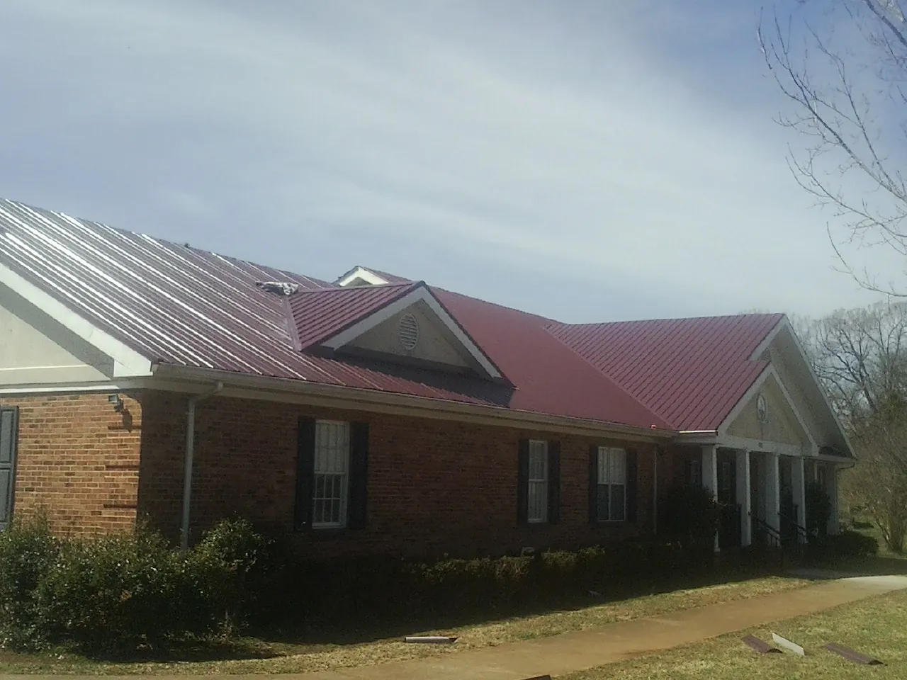 Red metal roof with gabled entries on a long brick building, from a Hail Damage Roof Repair job in Millen