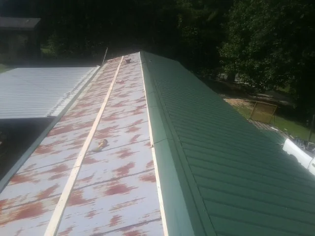 Old rusted panels beside newly installed green metal roofing — Wind Damage Roof Repair by Roofing Brothers in Millen