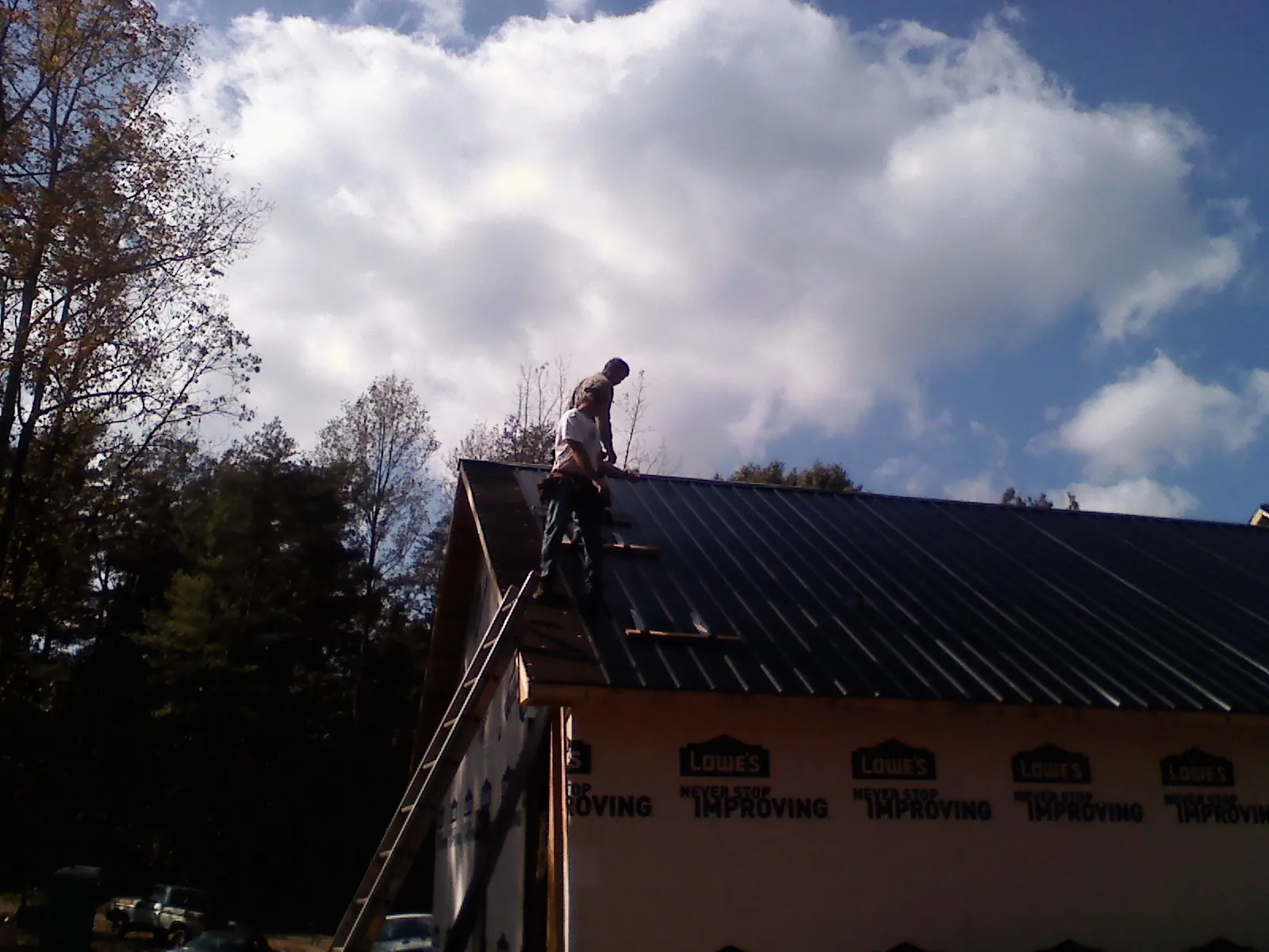 Roofer fastening dark metal panels high against a cloudy sky, from a Roof Inspection job in Millen