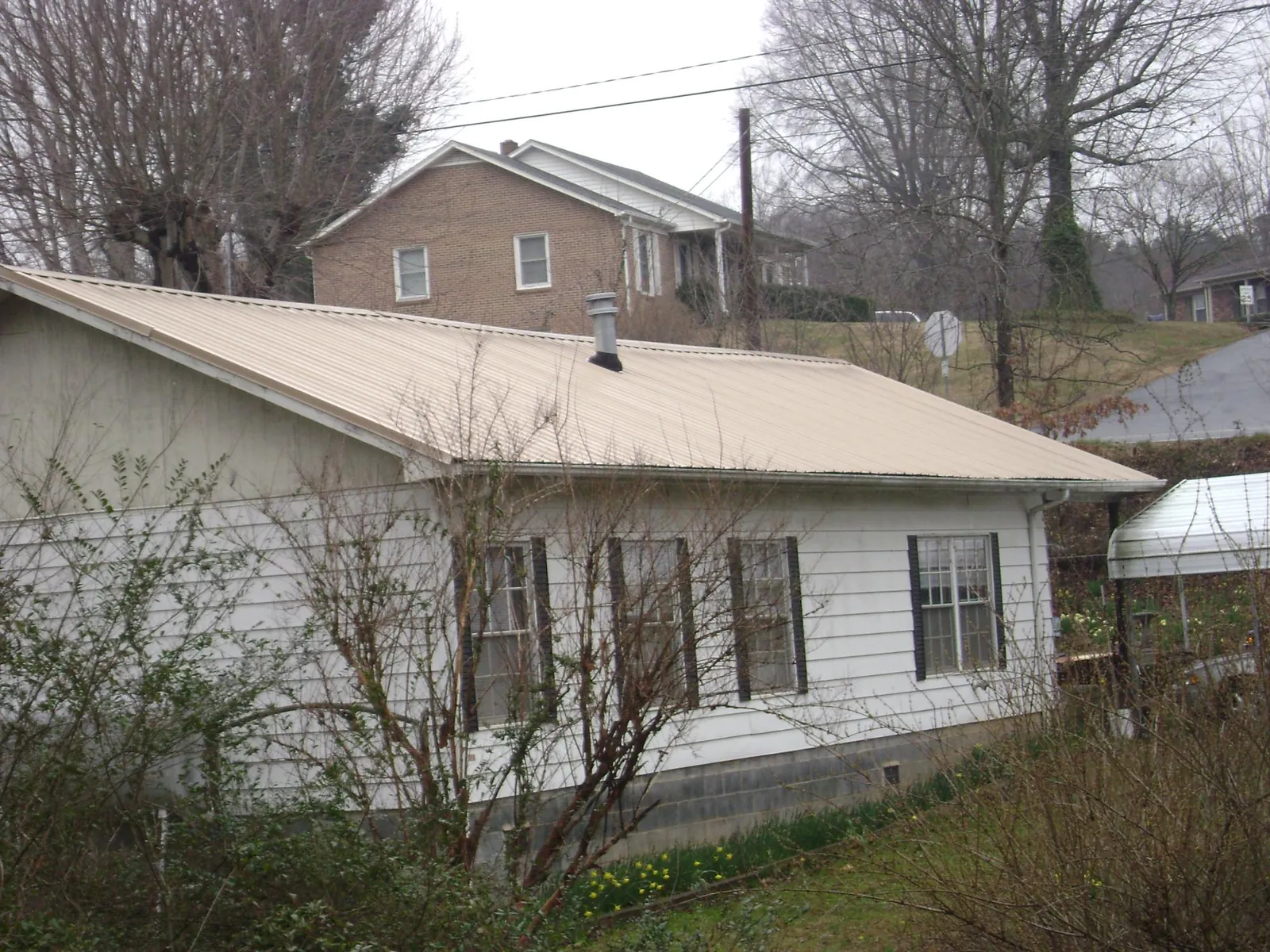 Tan metal roof on a white sided house set into a hillside — Commercial Roofing by Roofing Brothers in Millen